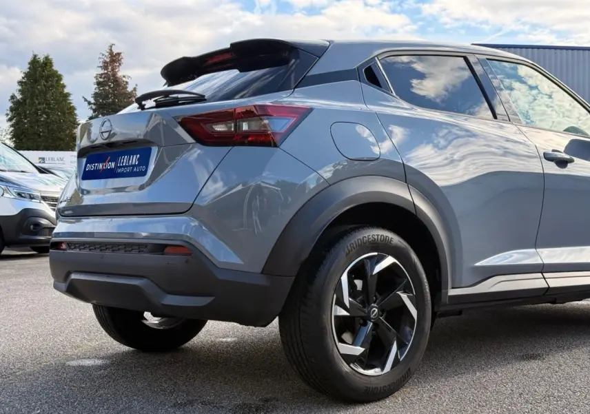 Vue 3/4 arrière droite du Nissan Juke gris clair 2023 avec jantes noires et feux arrière LED distinctifs.