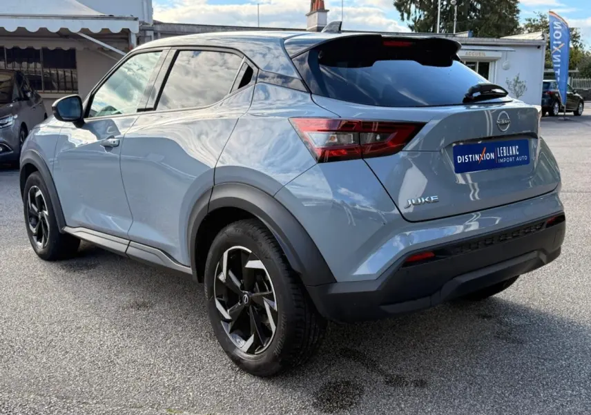 Vue 3/4 arrière droite d'un Nissan Juke gris clair 2023 avec jantes noires et toit noir brillant.