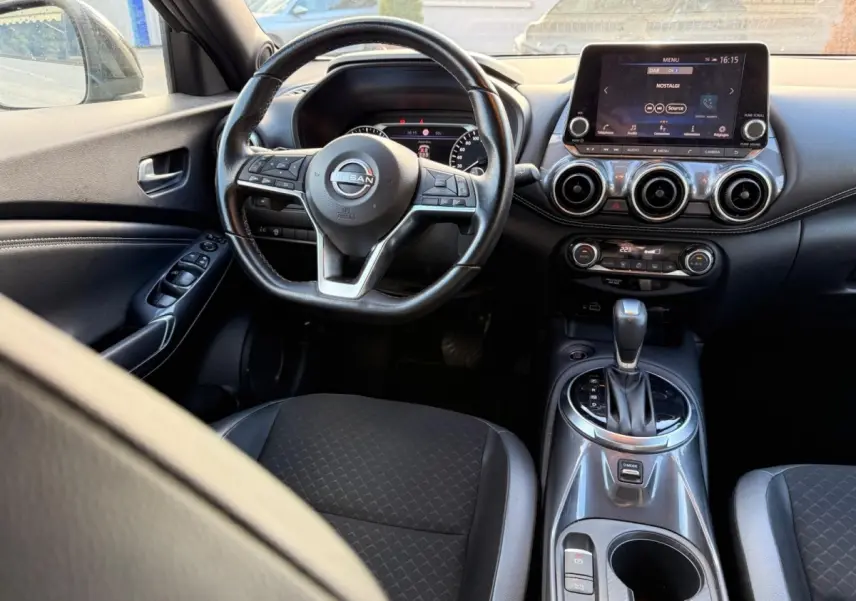 Vue intérieure avant du Nissan Juke gris clair 2023, volant cuir multifonctions et écran tactile central visible.
