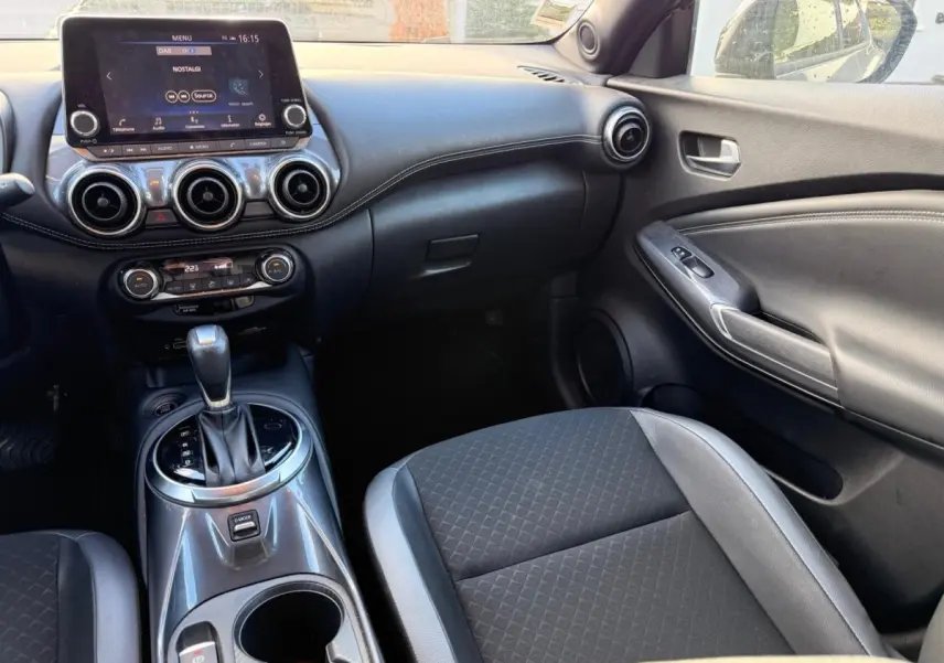 Vue intérieure côté passager du tableau de bord et console centrale du Nissan Juke gris clair avec écran tactile et levier de boîte auto.