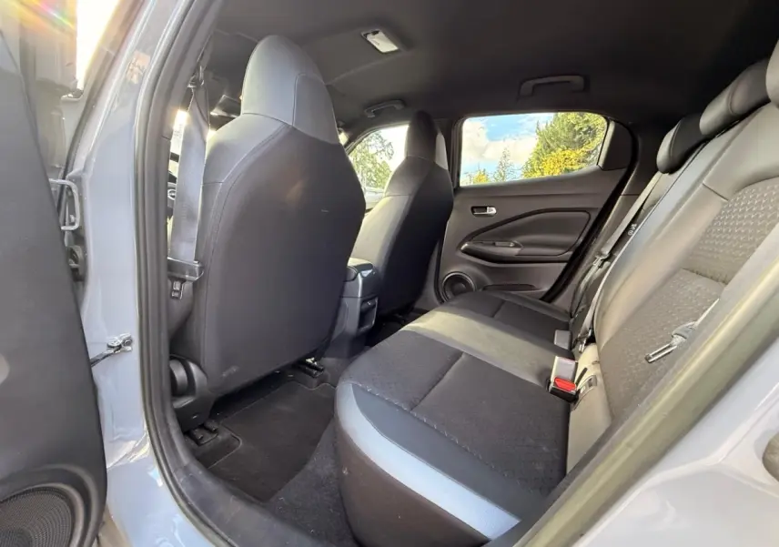 Vue intérieure arrière côté droit du Nissan Juke gris clair 2023, montrant la banquette 3 places et les dossiers des sièges avant.