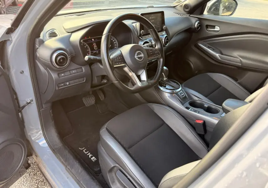 Intérieur côté conducteur du Nissan Juke gris clair 2023, volant cuir multifonctions et écran tactile central visible.