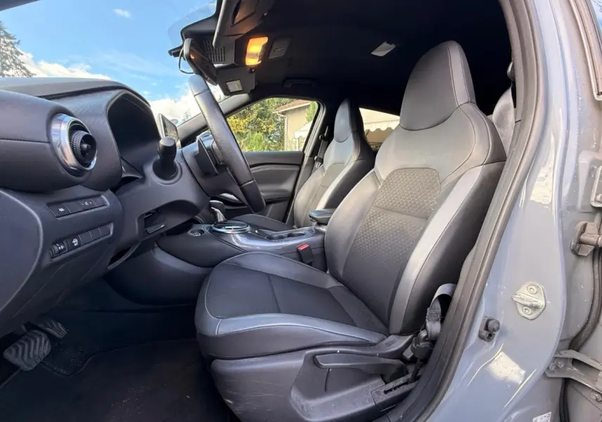 Vue intérieure côté conducteur du Nissan Juke gris clair 2023, mettant en valeur les sièges avant et le tableau de bord.