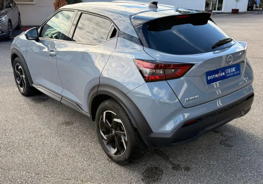 Vue 3/4 arrière droite d'un Nissan Juke gris clair 2023 avec vitres teintées et jantes noires distinctives.