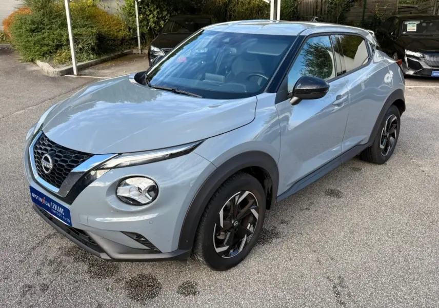 Nissan Juke gris clair en vue 3/4 avant droit, avec calandre noire et jantes alliage bicolores distinctives.