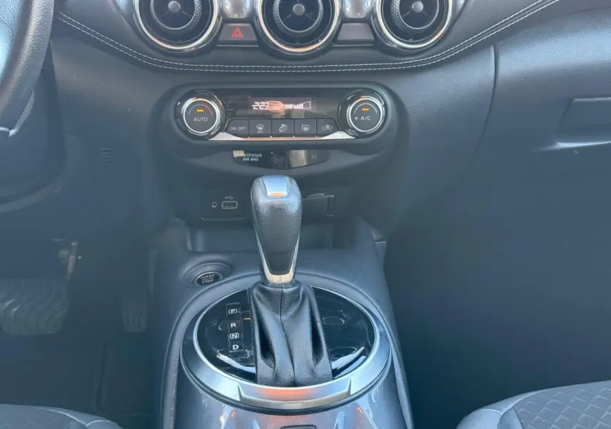 Vue intérieure centrée sur la console centrale noire du Nissan Juke 2023 avec levier de boîte auto et commandes climatisation.