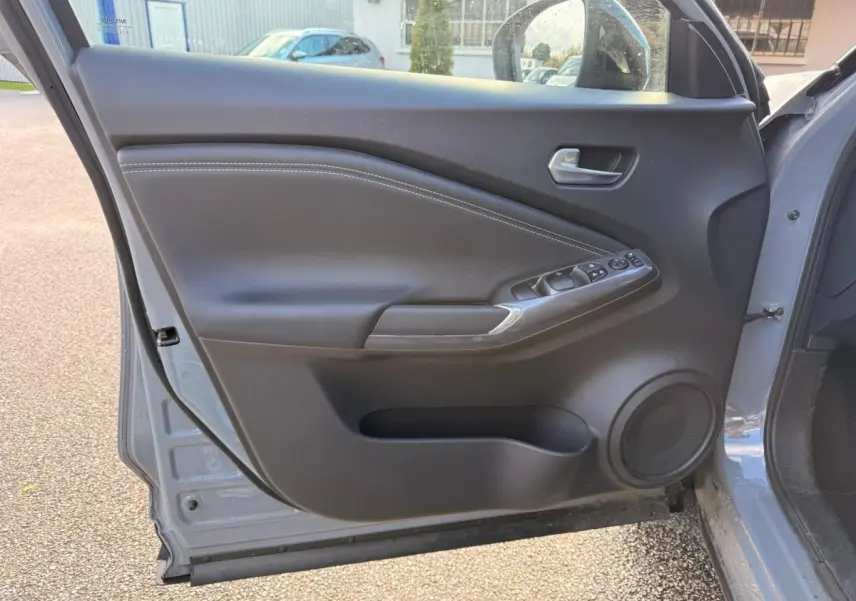Vue intérieure de la porte avant gauche gris clair du Nissan Juke 2023 avec commandes électriques et haut-parleur intégré.