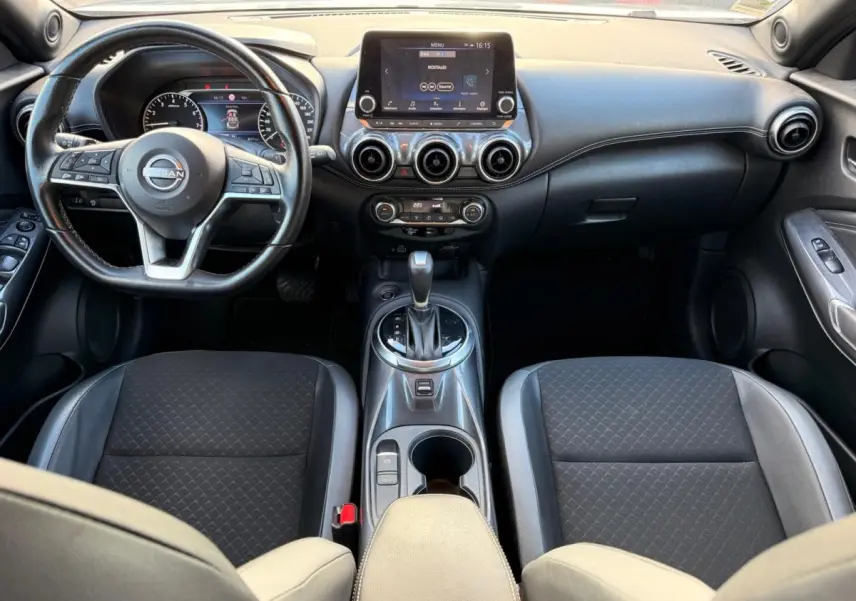 Vue intérieure avant du Nissan Juke 2023 avec tableau de bord noir, écran tactile central et volant cuir multifonctions.