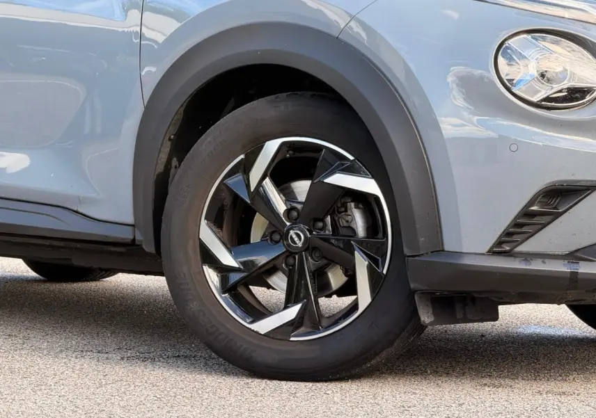 Gros plan sur la roue avant droite et le phare d'un Nissan Juke gris clair avec jante noire et argentée.