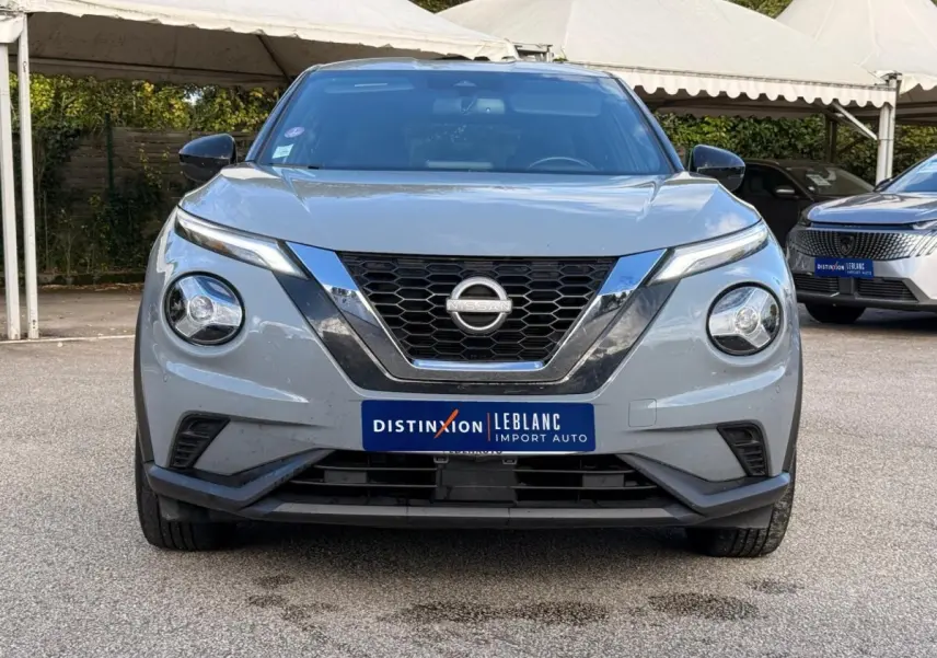 Vue de face d'un Nissan Juke gris clair 2023 avec calandre en V chromée et phares ronds LED distinctifs.