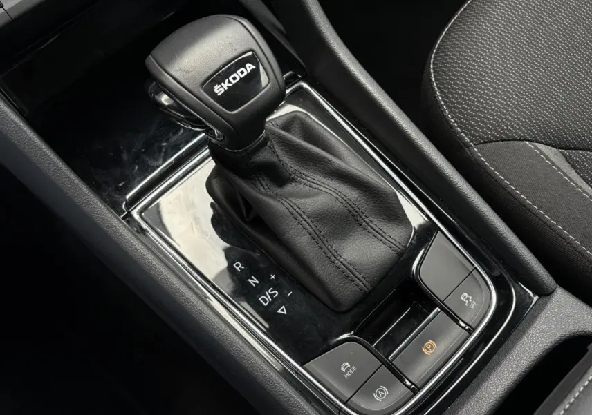 Le levier de vitesses automatique noir avec logo ŠKODA, entouré de commandes, intérieur tissu gris du ŠKODA KODIAQ 2024.