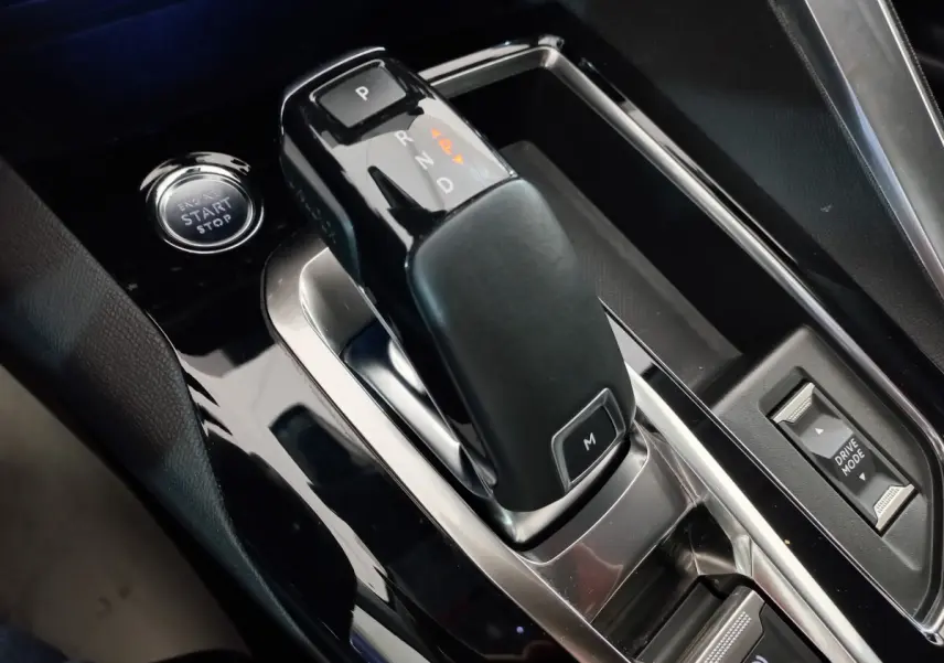 Gros plan sur la commande de boîte automatique noire et bouton start/stop du Peugeot 5008 gris foncé, intérieur moderne.