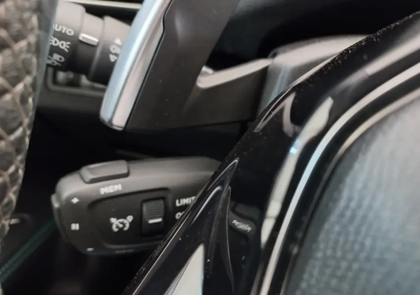 Gros plan sur la commande de régulateur de vitesse et limiteur, volant cuir noir du Peugeot 5008 gris foncé.