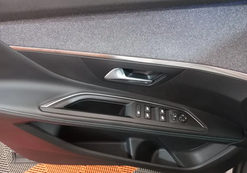Gros plan sur la porte côté gauche du Peugeot 5008 gris foncé, montrant les commandes des vitres et la poignée intérieure.