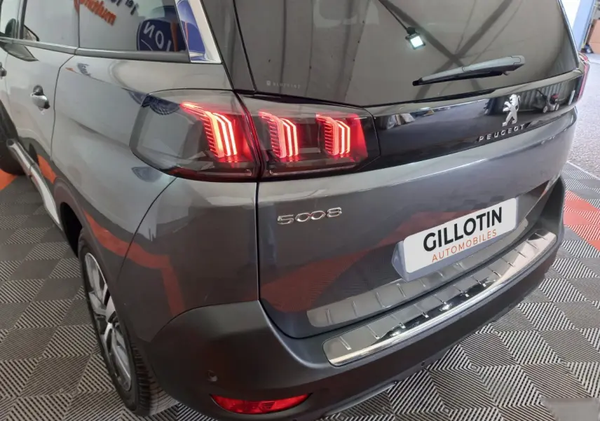 Vue 3/4 arrière droite d'un Peugeot 5008 gris foncé avec feux arrière LED allumés et logo visible.