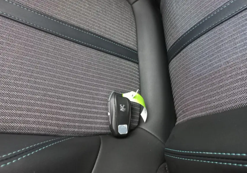 Gros plan sur la clé Peugeot posée sur un siège tissu gris à motifs chevrons avec surpiqûres bleues.