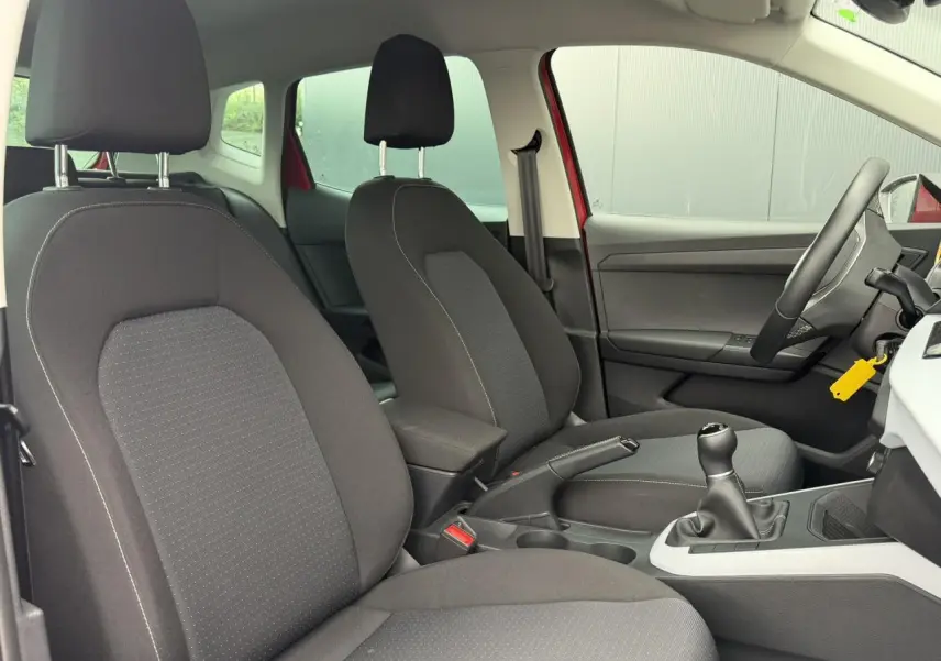 Vue intérieure côté conducteur du SEAT Arona rouge, mettant en valeur les sièges avant en tissu noir et la boîte manuelle.