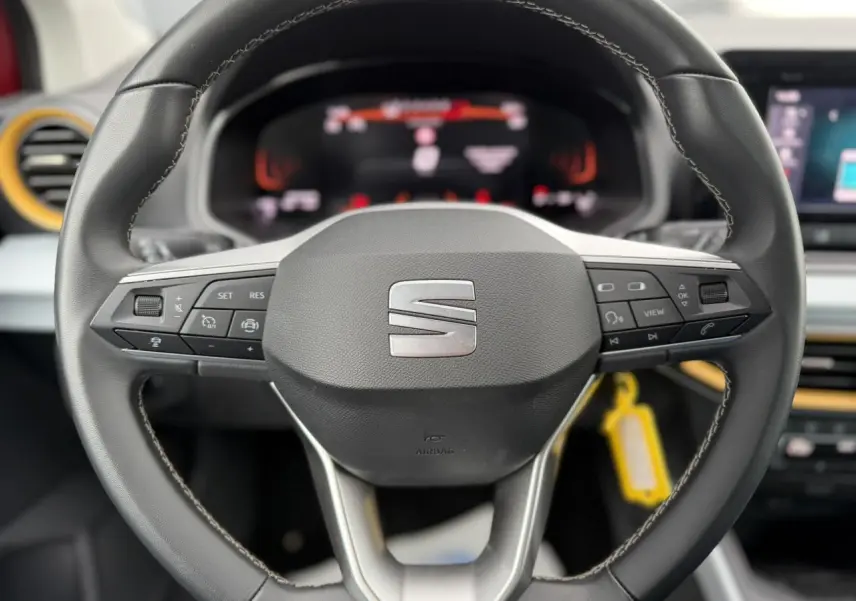 Gros plan sur le volant noir du SEAT Arona 2025 avec commandes intégrées et tableau de bord digital flou en arrière-plan.