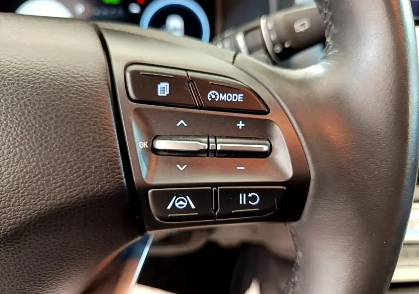 Gros plan sur les commandes multifonctions du volant cuir à droite du Hyundai Kona électrique bleu 2023.