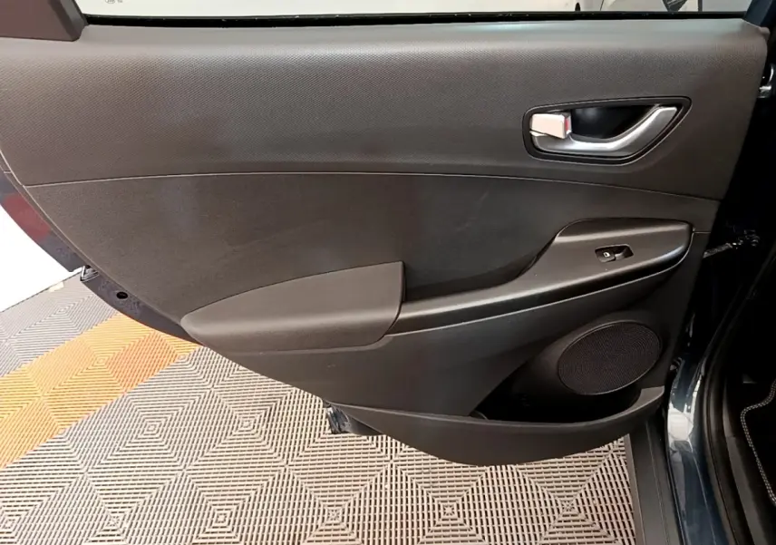 Vue intérieure de la porte arrière droite du Hyundai Kona bleu 2023 avec panneau noir et commande de vitre électrique.