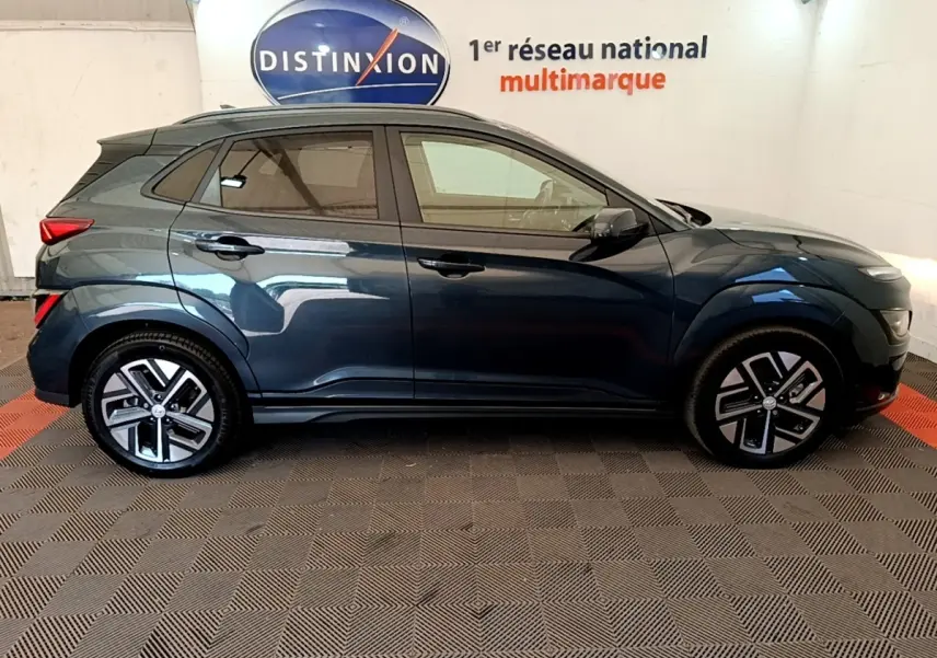 Vue latérale gauche d'un Hyundai Kona électrique bleu 2023 avec jantes alliage et rétroviseurs noirs.