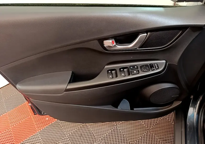 Vue rapprochée de la porte avant gauche intérieure noire avec commandes électriques et haut-parleur Hyundai Kona 2023.