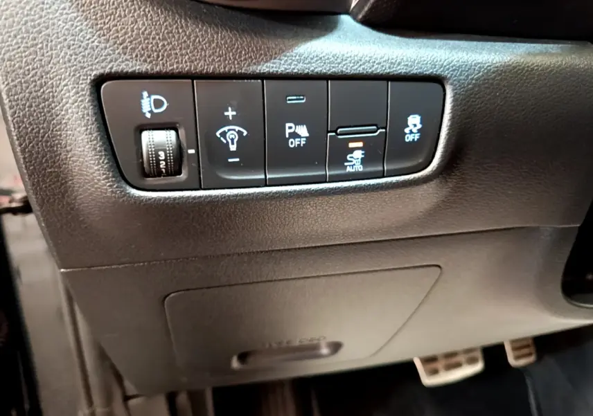 Vue rapprochée des commandes d’aide à la conduite et réglages lumineux sur la gauche du tableau de bord d’une Hyundai Kona électrique.