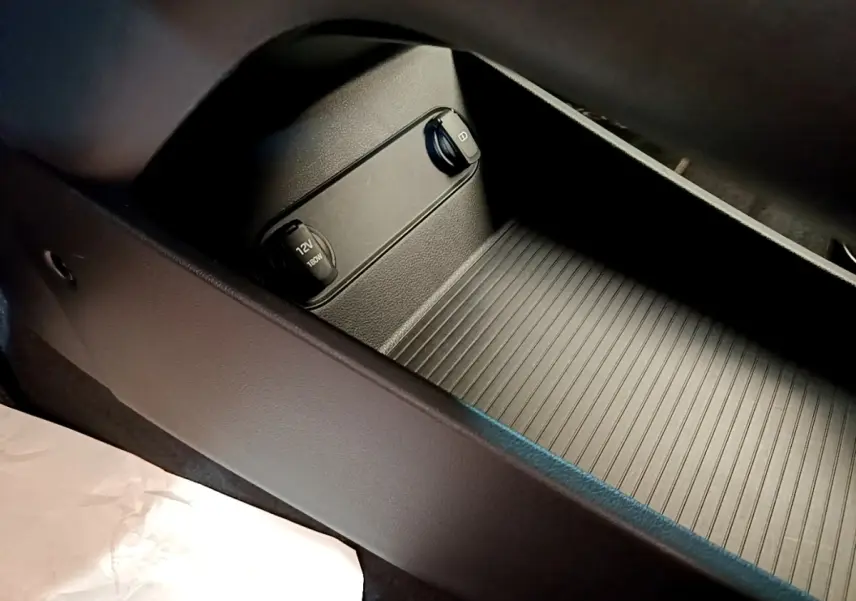 Gros plan sur la console centrale noire du Hyundai Kona électrique 2023 avec prise 12V et port USB.