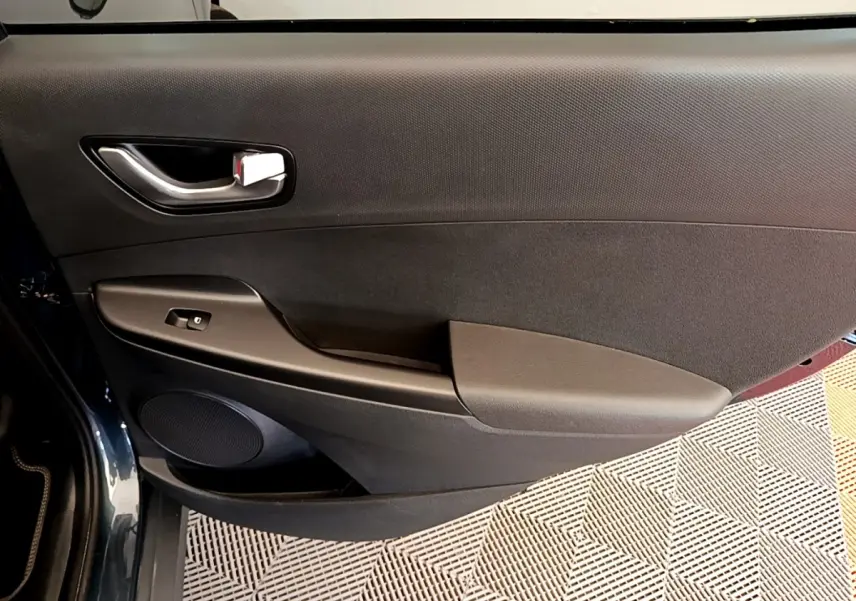Vue rapprochée de la porte avant gauche noire du Hyundai Kona électrique 2023 avec poignée argentée et commande de vitre.