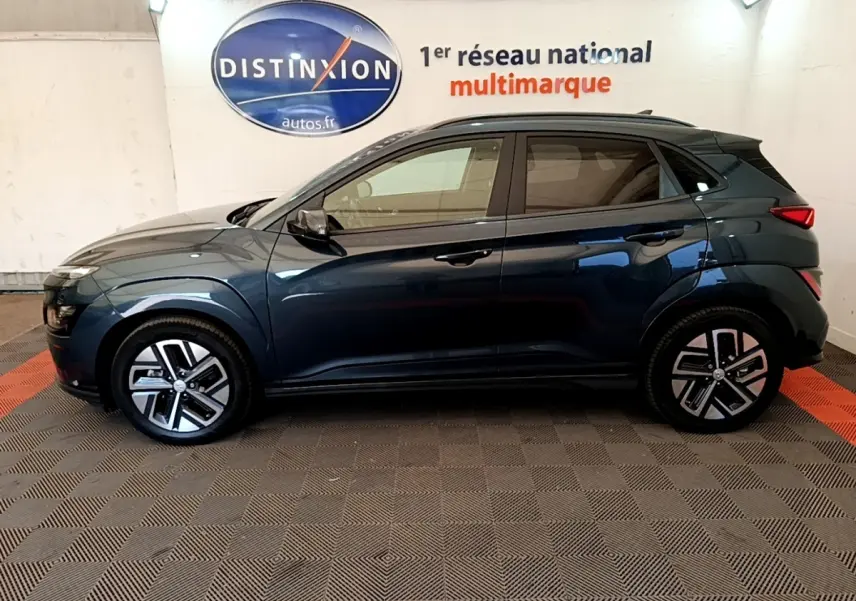 Vue latérale droite d'un Hyundai Kona électrique bleu 2023, avec jantes modernes et toit noir contrasté.