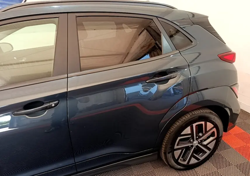 Vue latérale droite d'un Hyundai Kona électrique bleu foncé avec jantes spécifiques et poignées de porte intégrées.