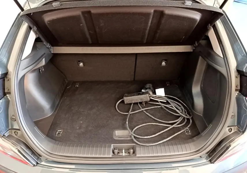 Vue arrière du coffre ouvert d’une Hyundai Kona électrique bleu avec câble de charge visible à l’intérieur.