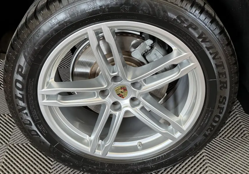 Gros plan sur la jante alu argentée avec logo Porsche au centre, montée sur pneu hiver Dunlop SP Winter Sport.