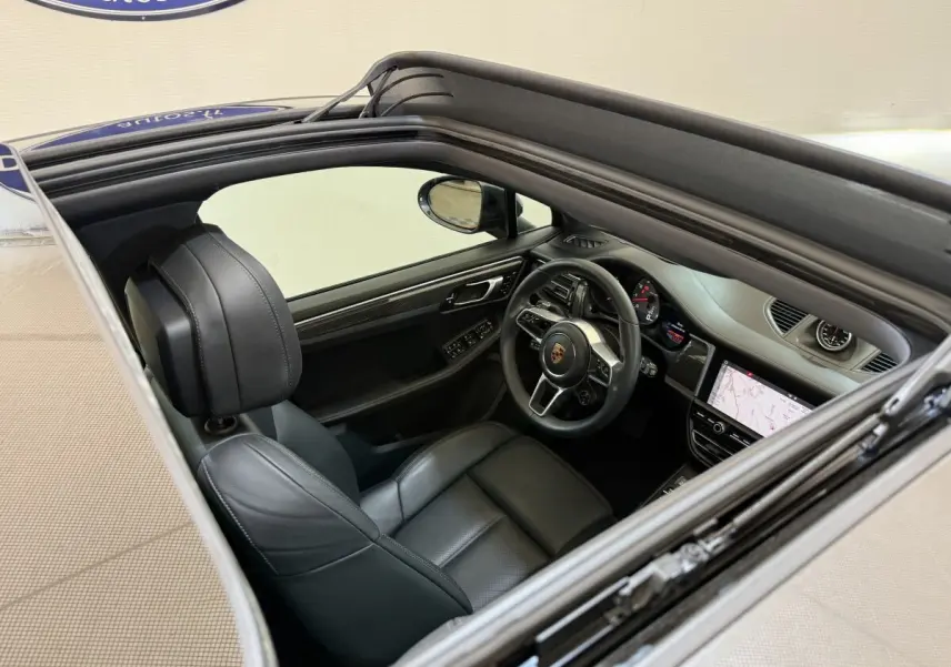 Vue intérieure par le toit ouvrant du Porsche Macan 3.0 S gris foncé, volant cuir alu et écran tactile de navigation visible.