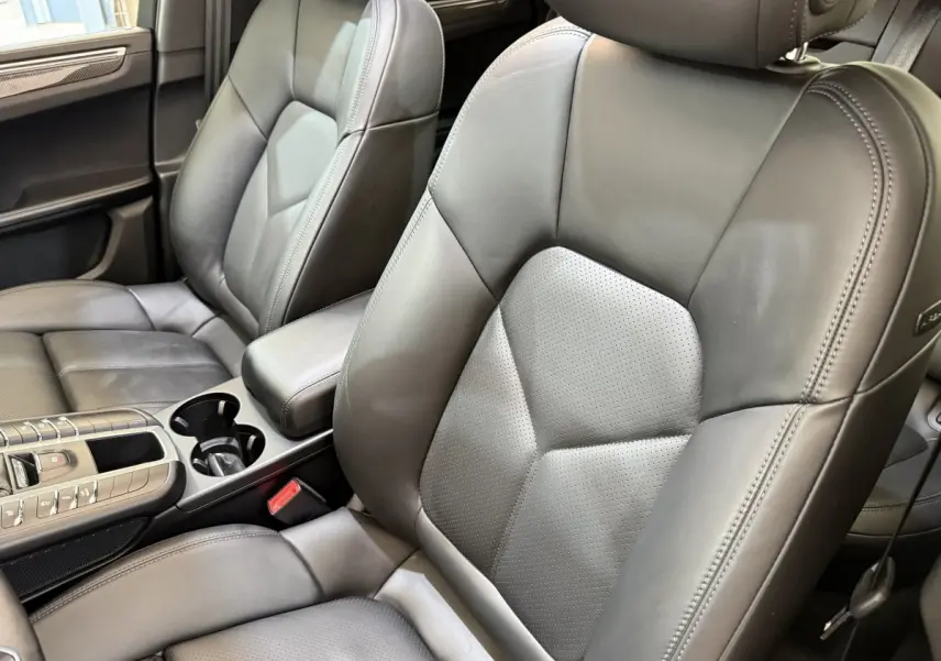 Gros plan sur les sièges avant en cuir gris foncé du Porsche Macan 3.0 S, avec console centrale et accoudoir visibles.