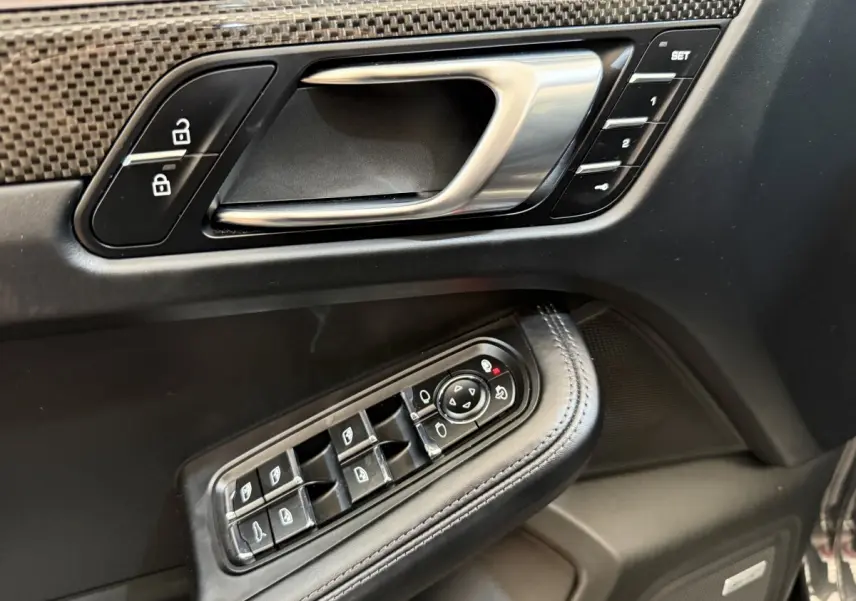 Gros plan sur la porte côté conducteur du Porsche Macan 3.0 S gris foncé, avec commandes alu et cuir, boutons mémoire et vitres.