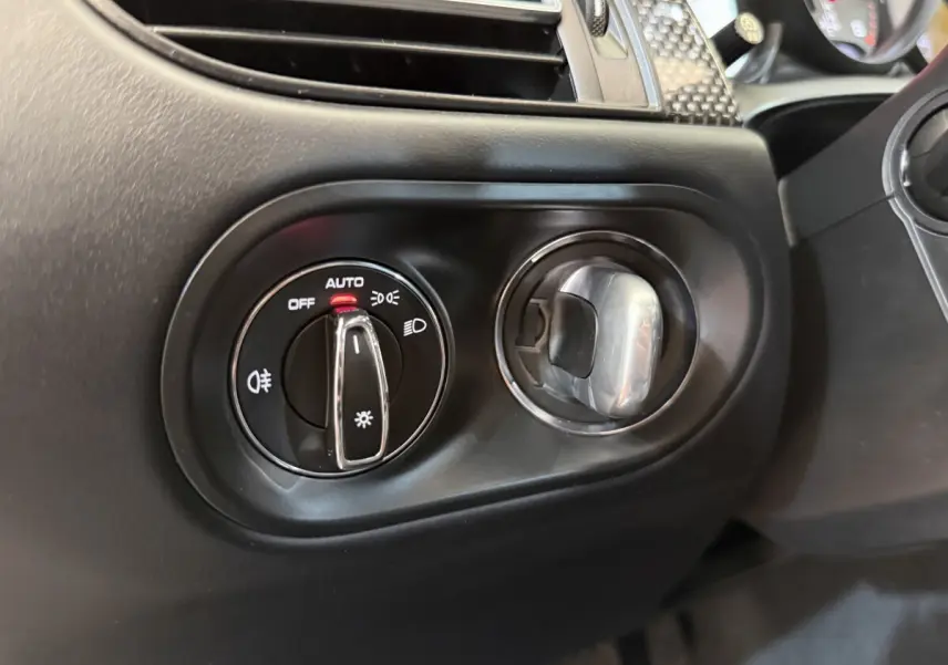 Gros plan sur la commande des phares et l'aération côté gauche du tableau de bord noir du Porsche Macan 3.0 S 2019.