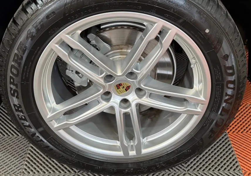 Gros plan sur la jante alu argentée avec logo Porsche au centre, montée sur pneu Dunlop hiver.