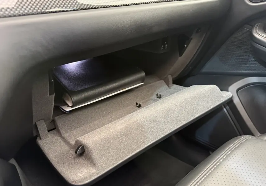 Vue intérieure côté passager du coffre à gants ouvert du Porsche Macan 3.0 S gris foncé avec dossier de siège en cuir perforé.