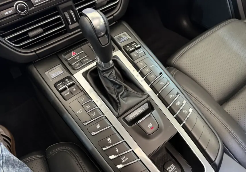 Gros plan sur la console centrale cuir noire du Porsche Macan 3.0 S avec levier de vitesse et commandes climatisation.