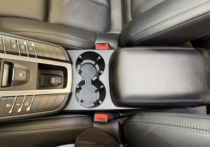 Vue plongeante sur la console centrale noire du Porsche Macan 3.0 S avec porte-gobelets et accoudoir cuir.