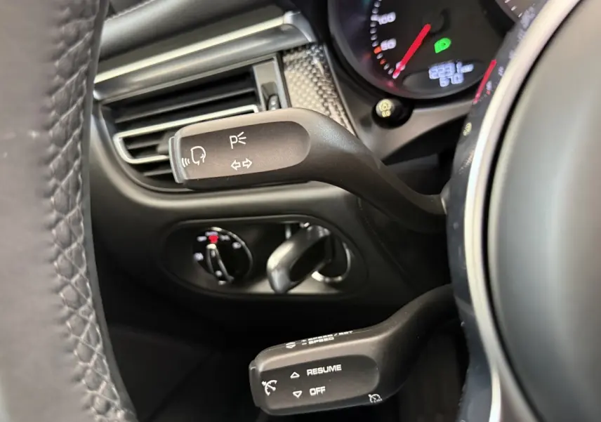 Gros plan sur les commandes au volant en cuir du Porsche Macan 3.0 S gris foncé, affichage du tableau de bord partiel visible.