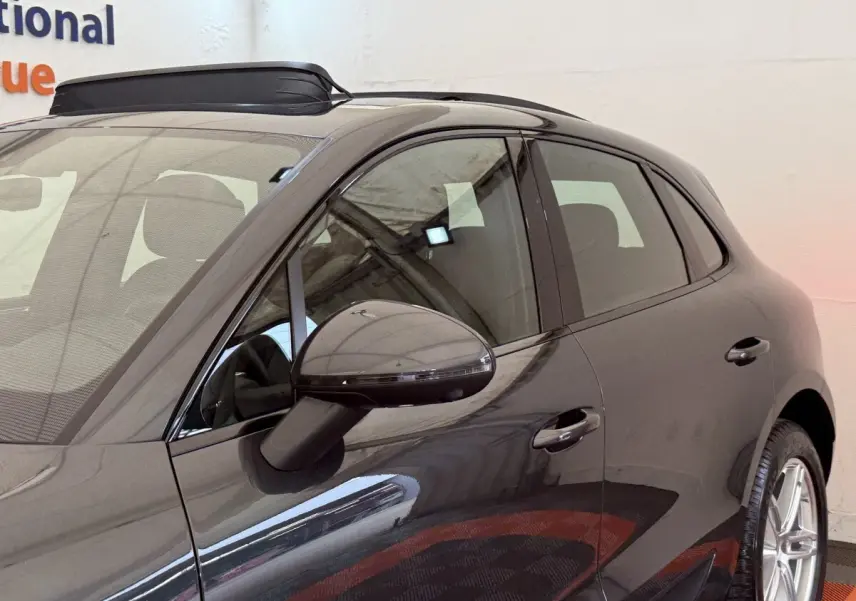 Vue latérale côté gauche d’un Porsche Macan 3.0 S gris foncé avec rétroviseur et poignées de porte visibles.
