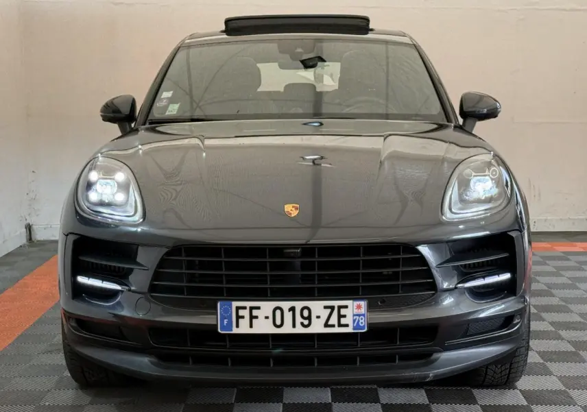 Vue frontale d’un Porsche Macan 3.0 S gris foncé avec phares LED allumés et calandre noire dans un garage.