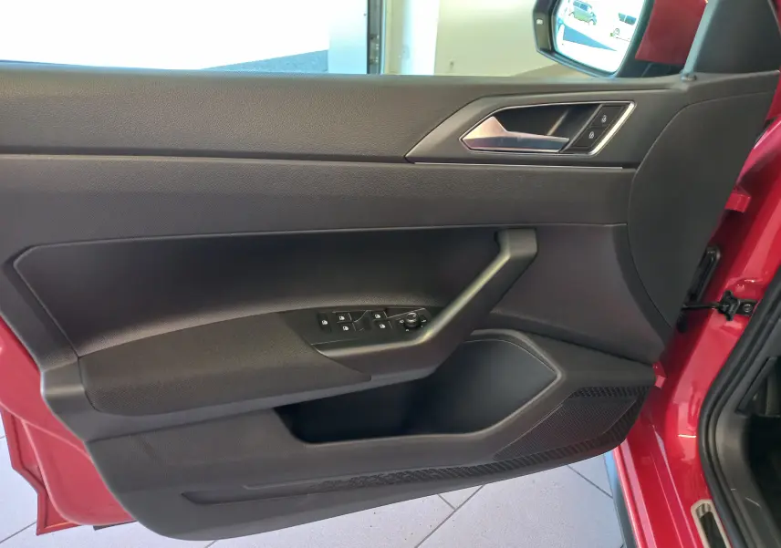 Vue intérieure du côté gauche de la porte avant d'une Volkswagen Polo Rouge Roi 2025, avec commandes de vitres et verrouillage.