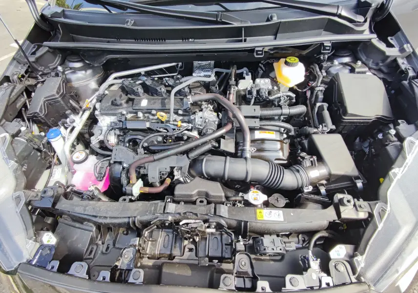 Vue plongeante sur le moteur essence hybride d'une Mazda2 2024 gris foncé, montrant les composants sous le capot ouvert.