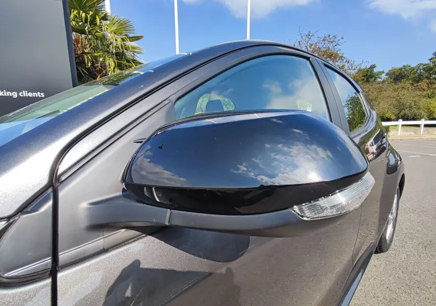 Rétroviseur côté gauche gris foncé du Mazda2 2024 Hybrid EXCLUSIVE LINE, reflétant le ciel et l'environnement extérieur.