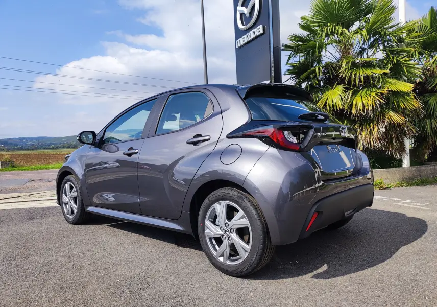 Vue 3/4 arrière droite d'une Mazda2 gris foncé 2024 garée devant un panneau Mazda avec palmiers en arrière-plan.