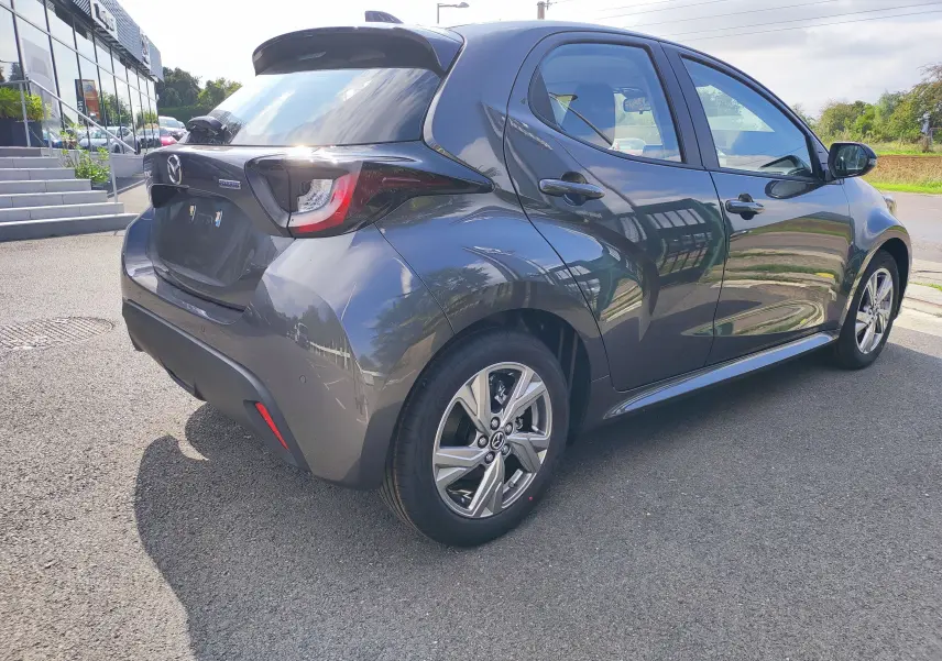 Vue 3/4 arrière droite d'une Mazda2 gris foncé 2024 hybride, avec jantes alliage et feux arrière distinctifs.