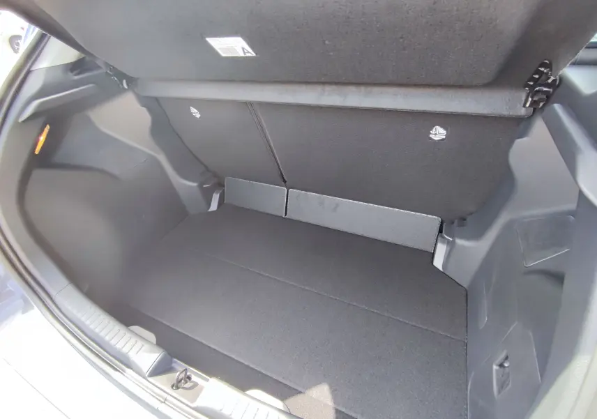 Coffre ouvert vu de l'arrière d'une Mazda2 1.5 Hybrid gris foncé, montrant un espace de chargement propre et spacieux.